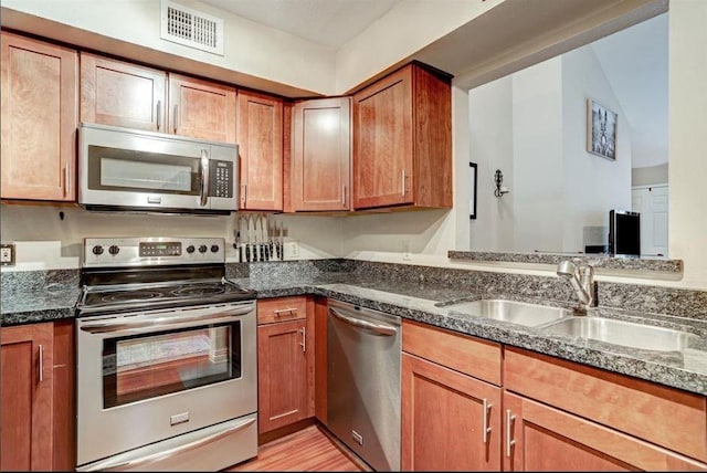 kitchen with dark stone countertops, sink, light hardwood / wood-style floors, and appliances with stainless steel finishes