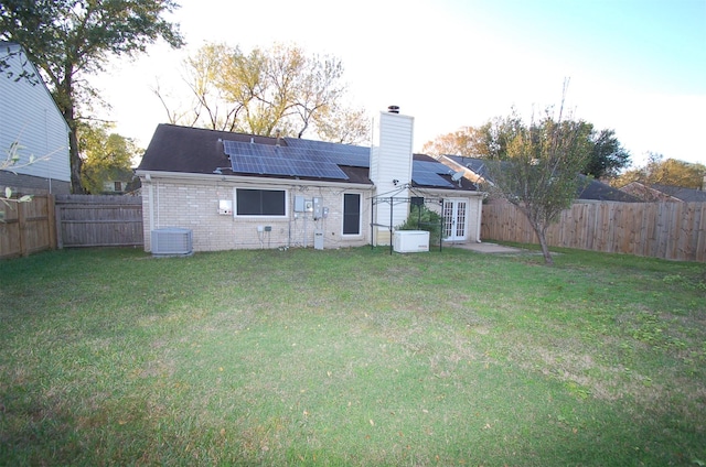 back of house featuring solar panels, central AC unit, and a lawn