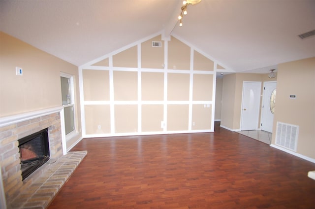 unfurnished living room featuring vaulted ceiling with beams, track lighting, a brick fireplace, and dark wood-type flooring