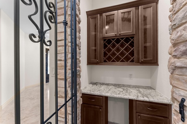 bar featuring built in desk, light stone counters, and dark brown cabinetry