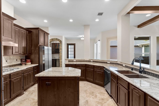 kitchen with light stone counters, dark brown cabinets, stainless steel appliances, sink, and a center island