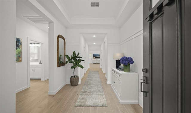 corridor with ornamental molding, plenty of natural light, and a tray ceiling