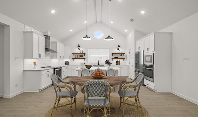 kitchen featuring hanging light fixtures, appliances with stainless steel finishes, white cabinets, wall chimney range hood, and backsplash