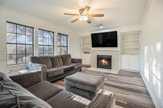 living room with a tile fireplace, wood-type flooring, a textured ceiling, and ornamental molding