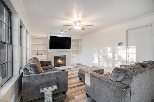 living room with ceiling fan, built in features, wood-type flooring, a textured ceiling, and ornamental molding