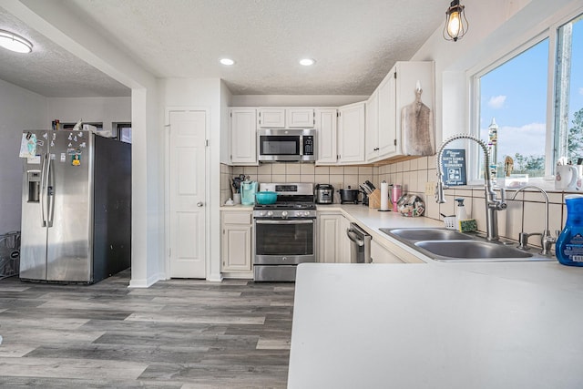 kitchen featuring a textured ceiling, stainless steel appliances, sink, white cabinets, and hardwood / wood-style floors