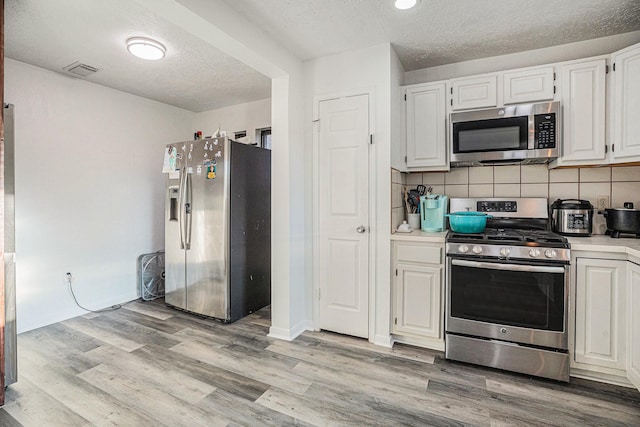 kitchen featuring decorative backsplash, white cabinetry, stainless steel appliances, and light wood-type flooring