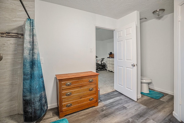 bathroom with hardwood / wood-style floors, a textured ceiling, toilet, and walk in shower