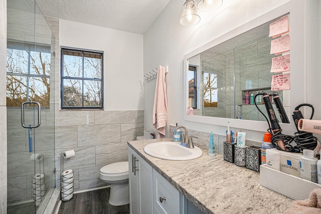 bathroom with wood-type flooring, a textured ceiling, toilet, vanity, and tile walls