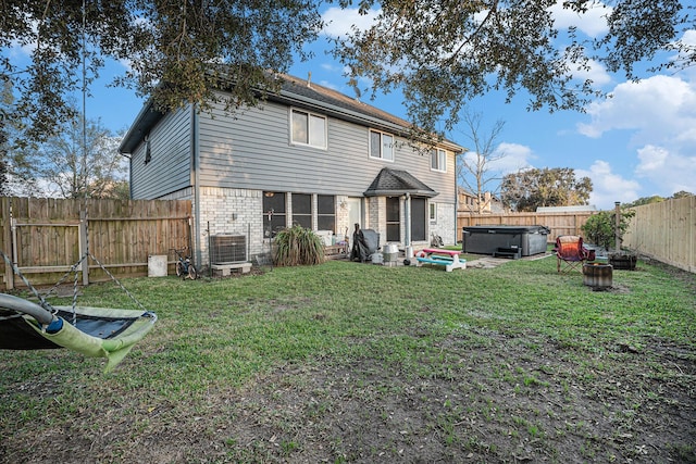 rear view of house with a lawn, cooling unit, and a hot tub