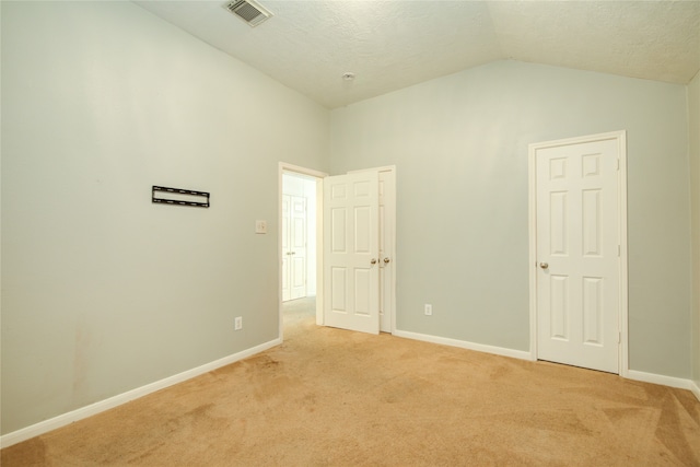 empty room featuring light carpet, a textured ceiling, and lofted ceiling