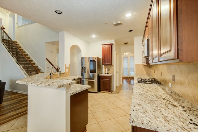 kitchen featuring sink, light wood-type flooring, a textured ceiling, appliances with stainless steel finishes, and light stone counters