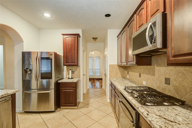 kitchen with a textured ceiling, stainless steel appliances, light stone counters, and light tile patterned flooring