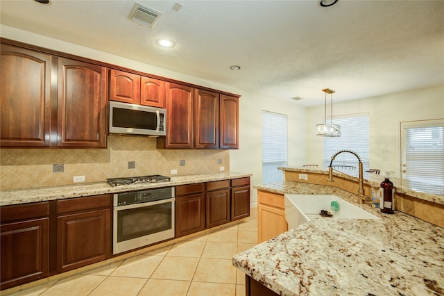 kitchen with light stone countertops, sink, stainless steel appliances, decorative light fixtures, and light tile patterned floors