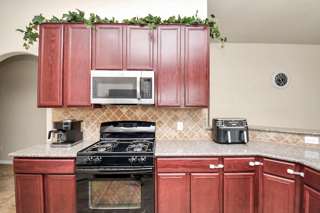 kitchen featuring black gas stove, tasteful backsplash, and light stone counters