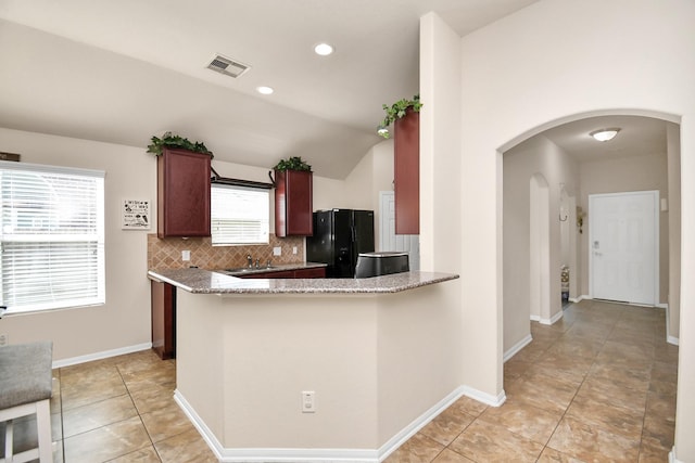 kitchen with black refrigerator, kitchen peninsula, plenty of natural light, and lofted ceiling