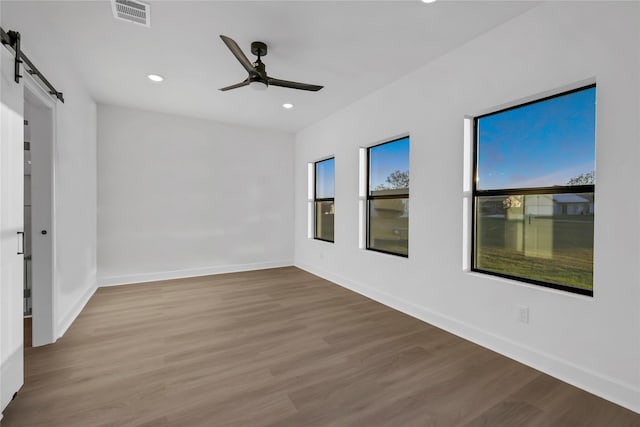 empty room with a barn door, ceiling fan, and hardwood / wood-style flooring