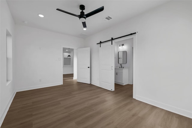 unfurnished bedroom featuring a barn door, ensuite bathroom, ceiling fan, and dark hardwood / wood-style floors