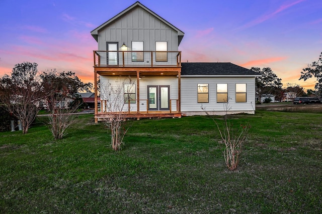 back house at dusk featuring a lawn, a balcony, and french doors