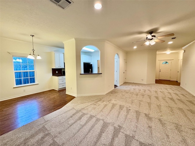 unfurnished living room featuring wood-type flooring, ceiling fan with notable chandelier, and crown molding