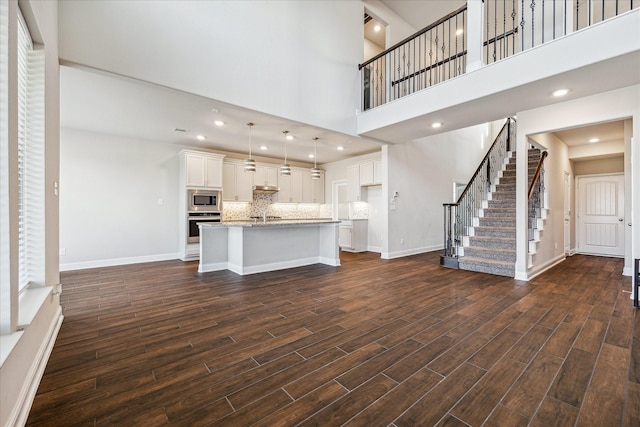 kitchen with a high ceiling, dark hardwood / wood-style floors, an island with sink, pendant lighting, and appliances with stainless steel finishes