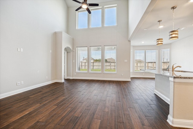 unfurnished living room with ceiling fan, dark wood-type flooring, and a high ceiling