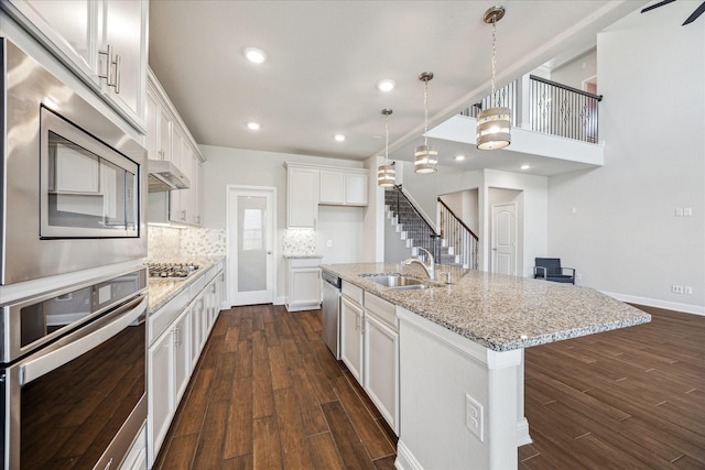 kitchen with pendant lighting, a kitchen island with sink, white cabinets, dark hardwood / wood-style floors, and stainless steel appliances