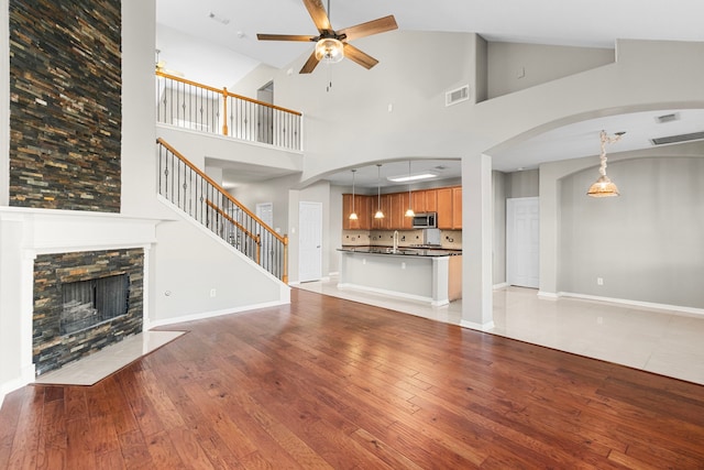 unfurnished living room featuring light wood-type flooring, ceiling fan, sink, high vaulted ceiling, and a fireplace