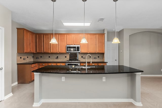 kitchen with hanging light fixtures, stainless steel appliances, tasteful backsplash, and a center island with sink