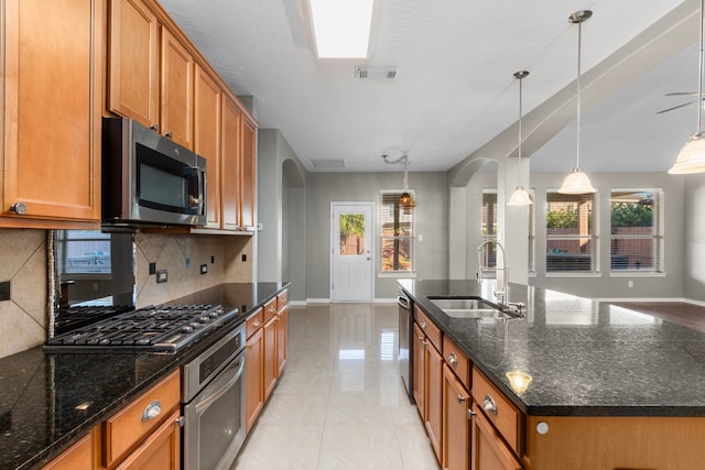 kitchen with a center island with sink, sink, decorative backsplash, appliances with stainless steel finishes, and decorative light fixtures