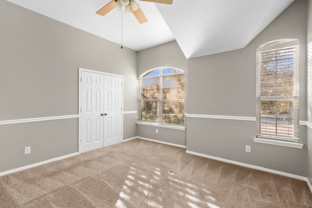 carpeted spare room featuring a wealth of natural light, lofted ceiling, and ceiling fan