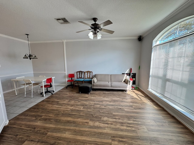 living room with hardwood / wood-style floors, ceiling fan with notable chandelier, crown molding, and a textured ceiling