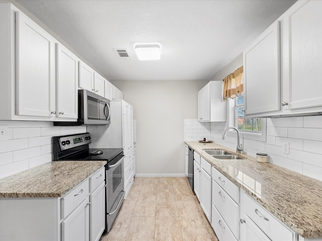 kitchen featuring white cabinetry, sink, light stone counters, and appliances with stainless steel finishes