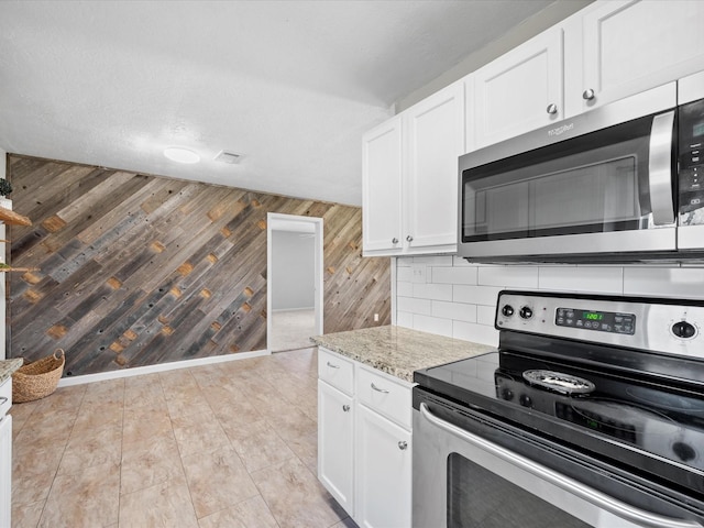 kitchen with wood walls, white cabinets, light stone countertops, a textured ceiling, and appliances with stainless steel finishes