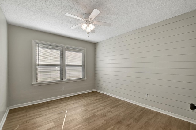 empty room with wood-type flooring, a textured ceiling, ceiling fan, and wood walls