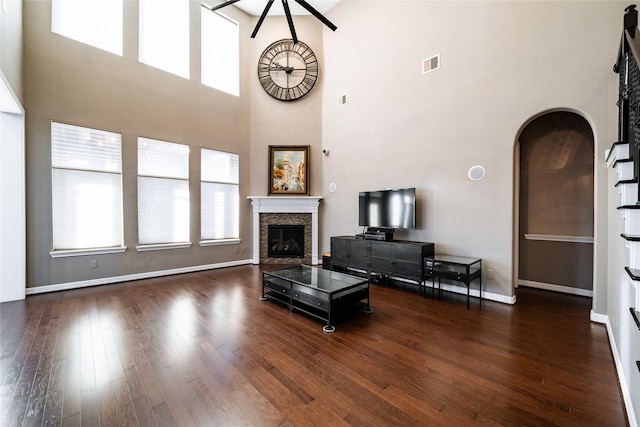 living room featuring a stone fireplace, a towering ceiling, and dark wood-type flooring