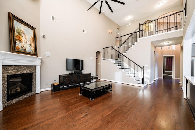 living room featuring ceiling fan, a fireplace, dark wood-type flooring, and a high ceiling