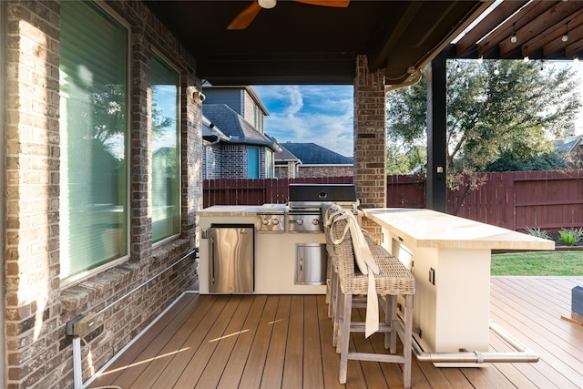 wooden deck featuring ceiling fan, a grill, a bar, and an outdoor kitchen