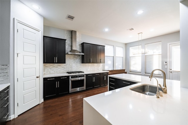 kitchen featuring sink, stainless steel appliances, wall chimney range hood, dark hardwood / wood-style floors, and decorative light fixtures