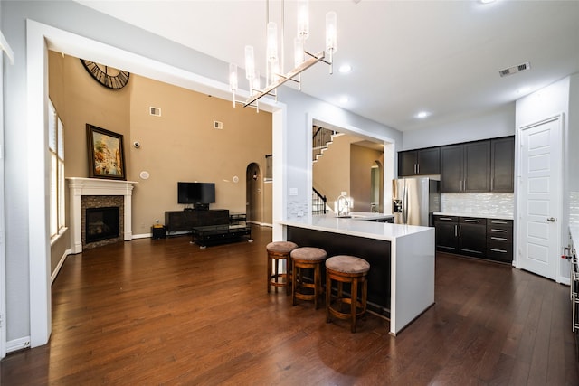 kitchen with a kitchen breakfast bar, a fireplace, decorative light fixtures, dark hardwood / wood-style flooring, and stainless steel fridge with ice dispenser