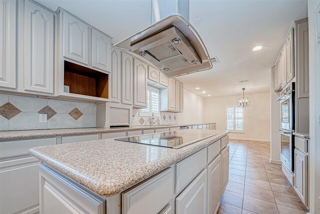 kitchen featuring black electric stovetop, tasteful backsplash, decorative light fixtures, a kitchen island, and white cabinetry