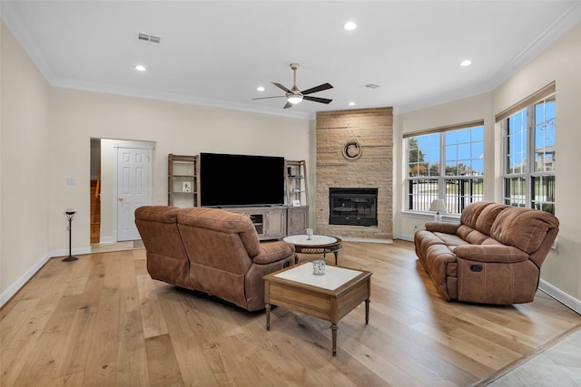 living room with ceiling fan, light hardwood / wood-style floors, a stone fireplace, and crown molding