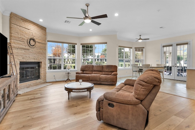 living room with french doors, crown molding, light hardwood / wood-style flooring, ceiling fan, and a fireplace