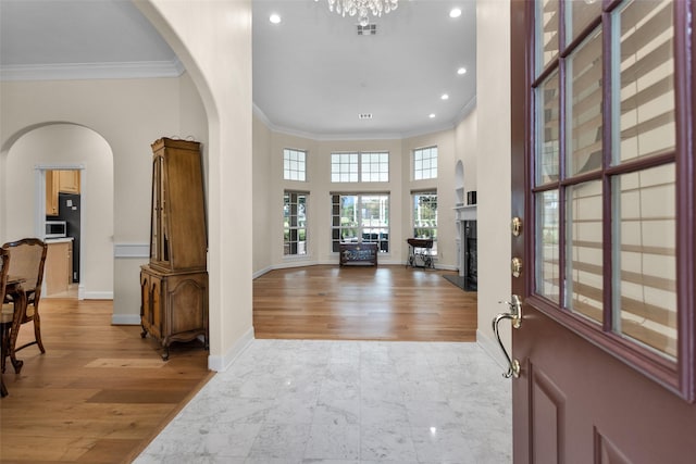 foyer entrance with a high end fireplace, ornamental molding, a towering ceiling, light hardwood / wood-style floors, and a chandelier