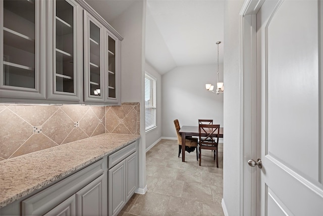 kitchen with an inviting chandelier, light stone counters, pendant lighting, vaulted ceiling, and decorative backsplash