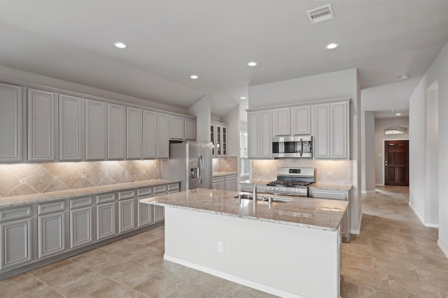 kitchen with gray cabinetry, sink, tasteful backsplash, an island with sink, and appliances with stainless steel finishes