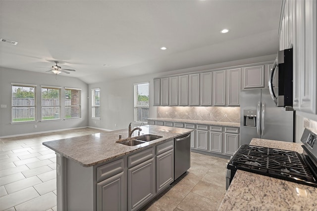 kitchen featuring lofted ceiling, a center island with sink, sink, decorative backsplash, and appliances with stainless steel finishes