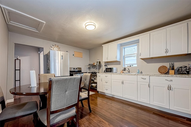 kitchen with light stone countertops, a textured ceiling, white cabinets, dark hardwood / wood-style floors, and stainless steel refrigerator