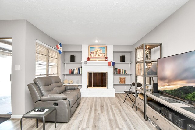 living room with a textured ceiling, light wood-type flooring, and a fireplace