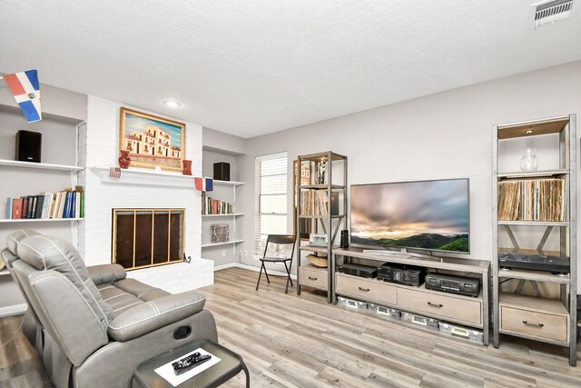 living room featuring a brick fireplace, a textured ceiling, and light wood-type flooring